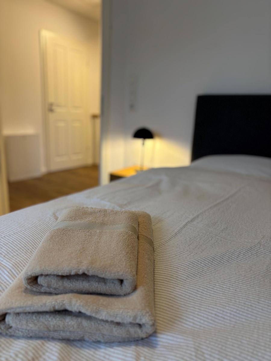 A bed with folded towels and a bedside lamp in the background.