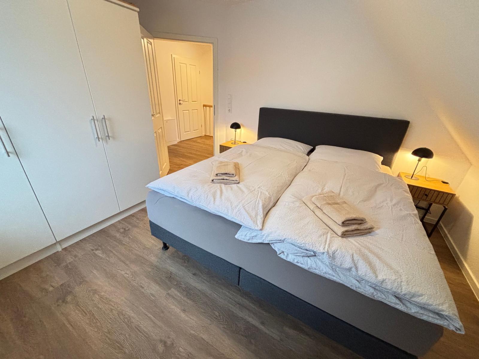 Bedroom with double bed, two nightstands, and wardrobe. Wooden floor and lamps.