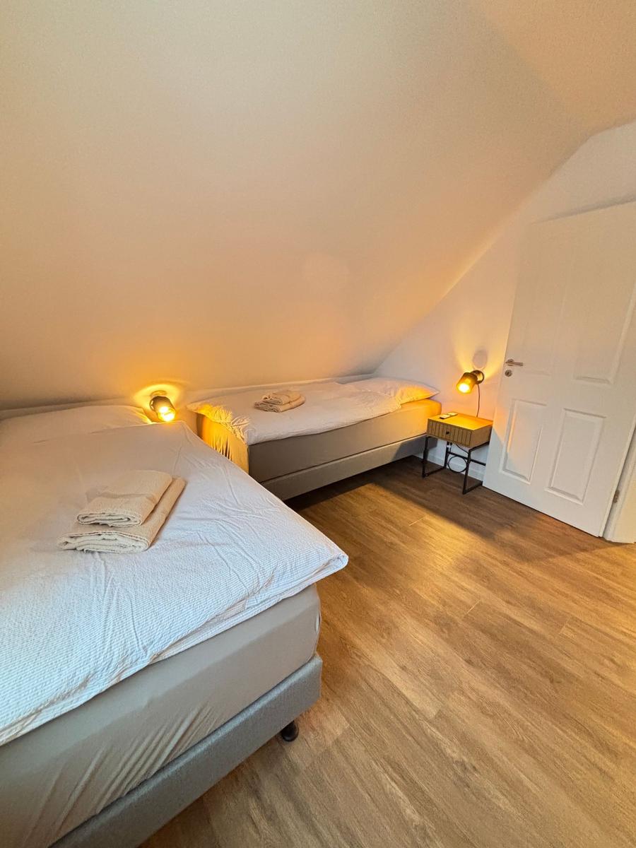 Two beds with white bedding and towels. Wooden floor and sloped ceiling.