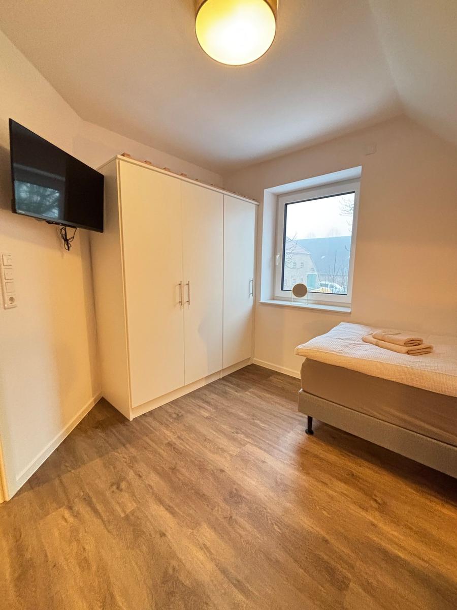 Bedroom with bed, wardrobe, and wall-mounted TV. Wooden floor and window with view.