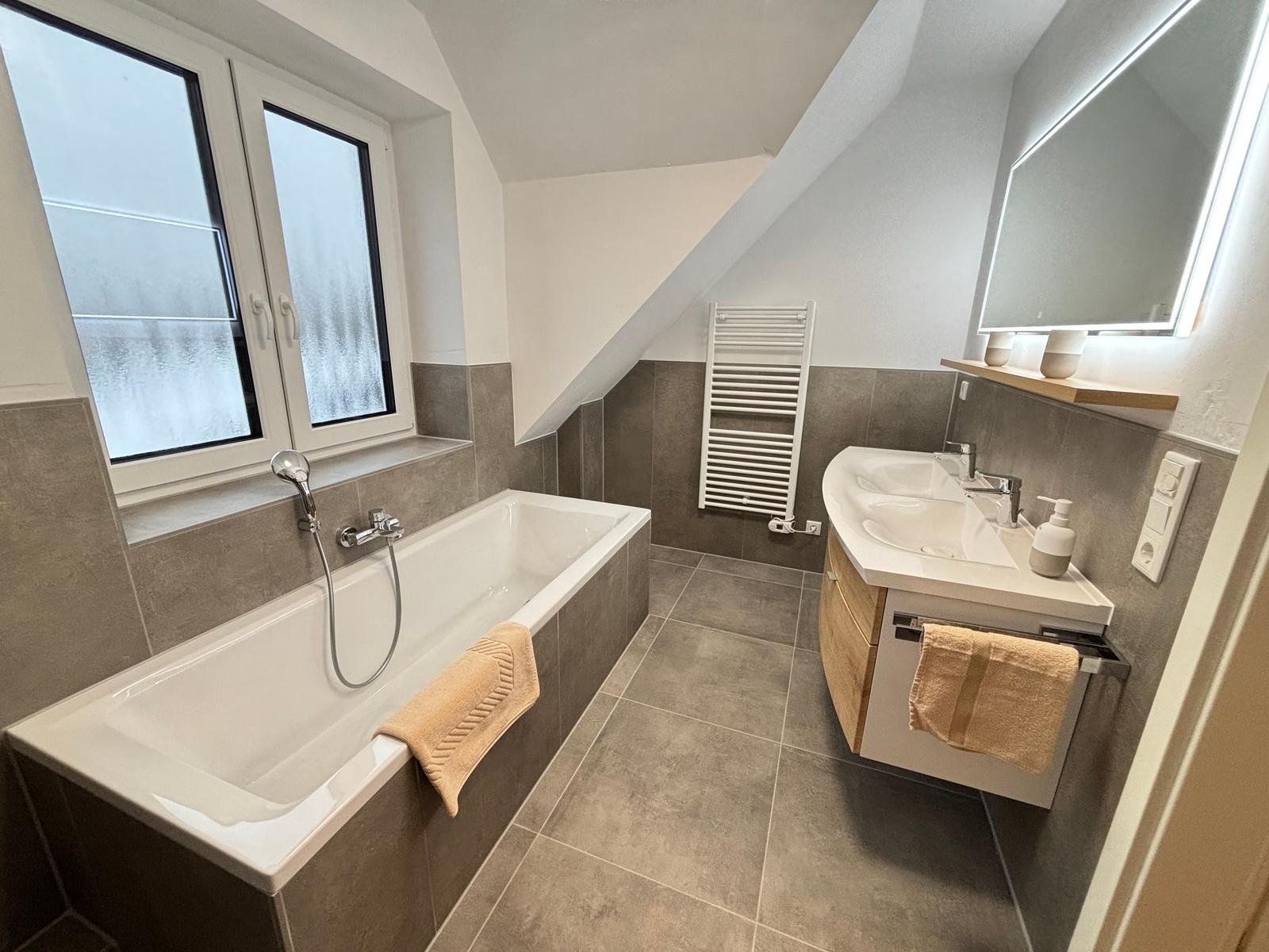 Bath with shower, sink and window. Sloped ceiling and gray tiles.