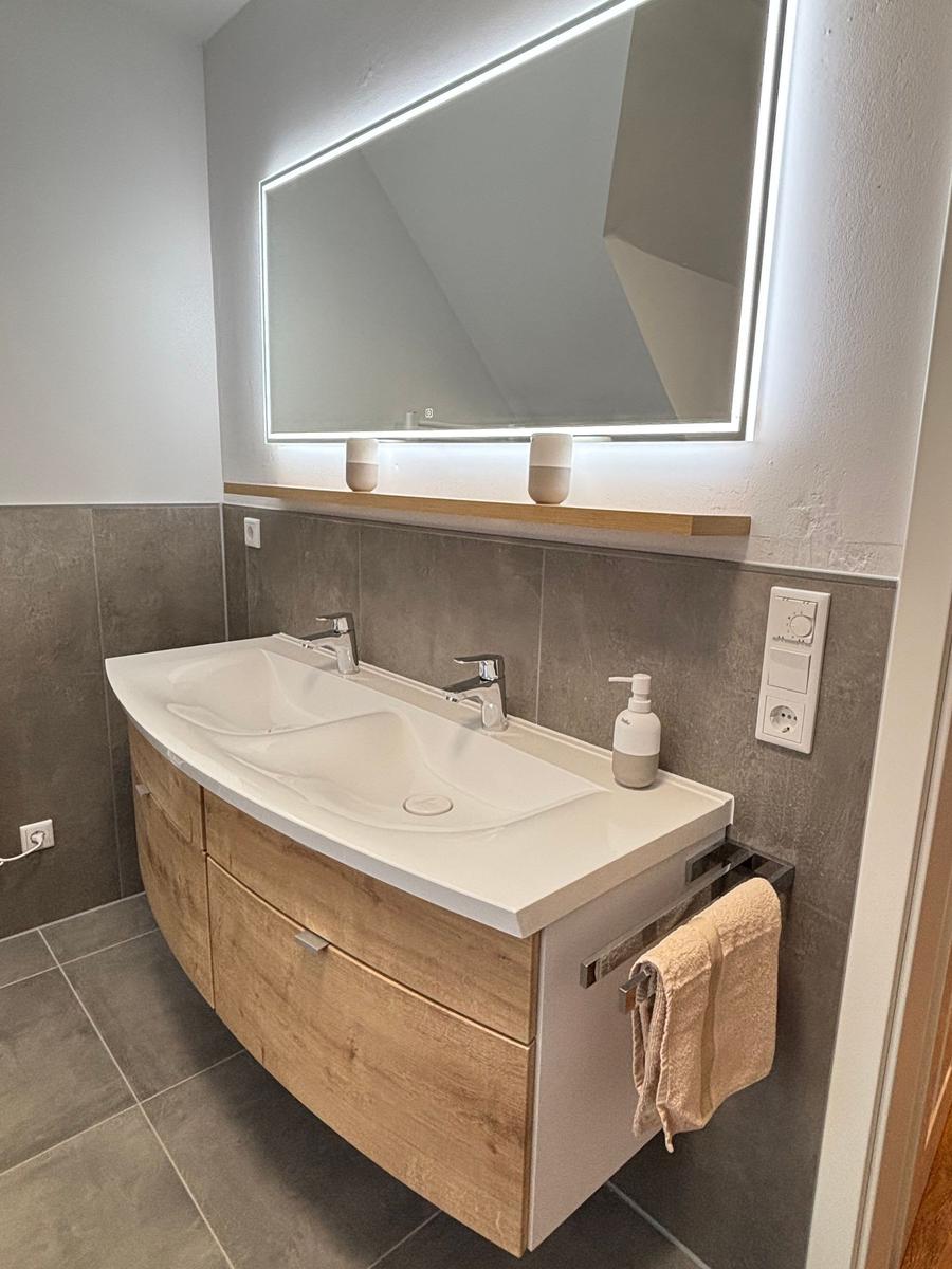 Bathroom with double sink, lit mirror, and wooden vanity.