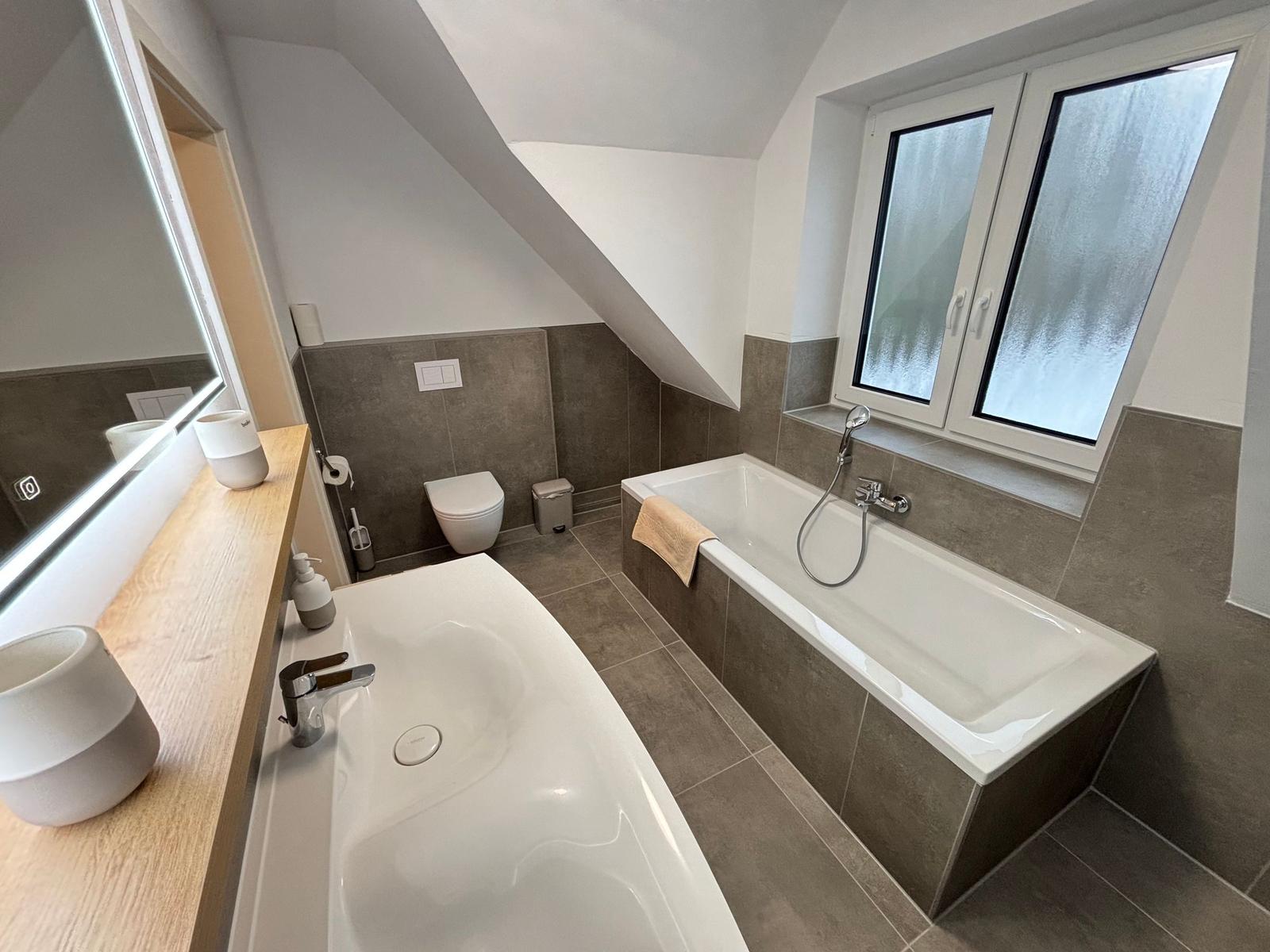 Bathroom with bathtub, sink, and toilet under sloped ceiling.