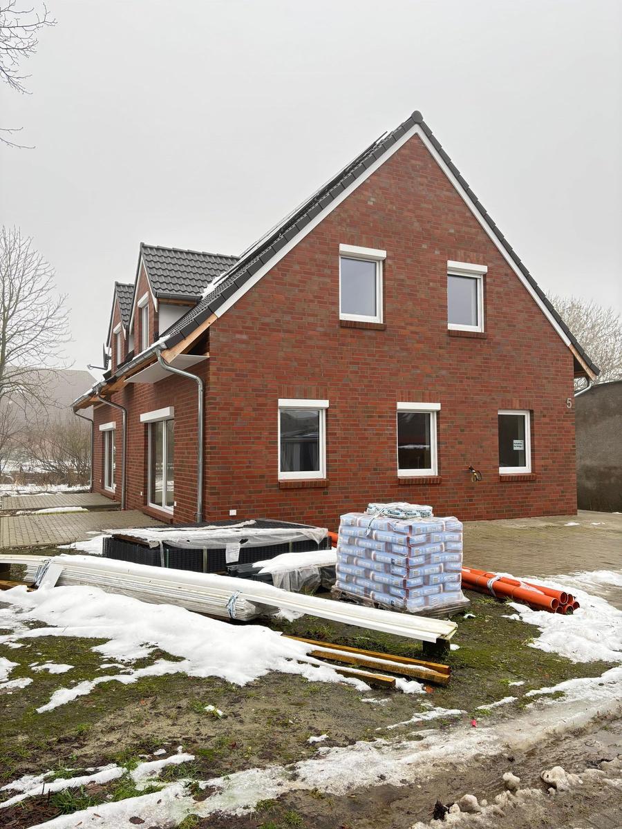 New build house with red brick facade and roof, construction materials in the garden.