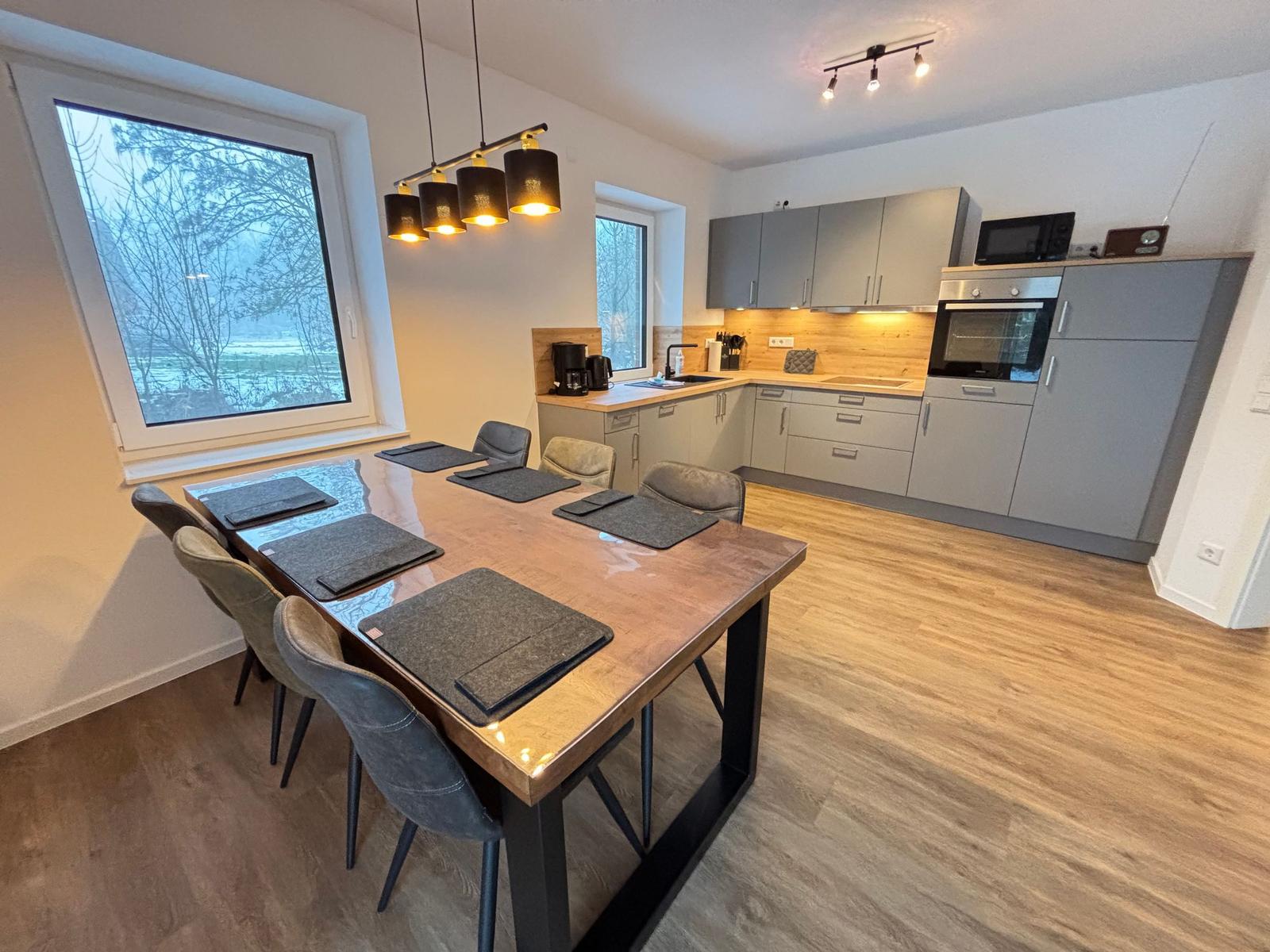 Dining area with table and chairs. Kitchen with worktop and appliances.