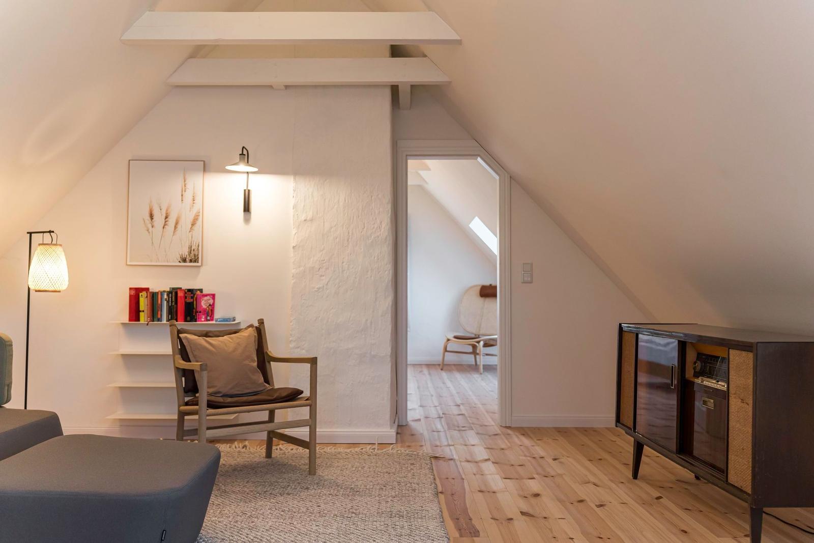 Dachgeschosszimmer mit Holzboden, Sessel, Schrank und Bücherregal.