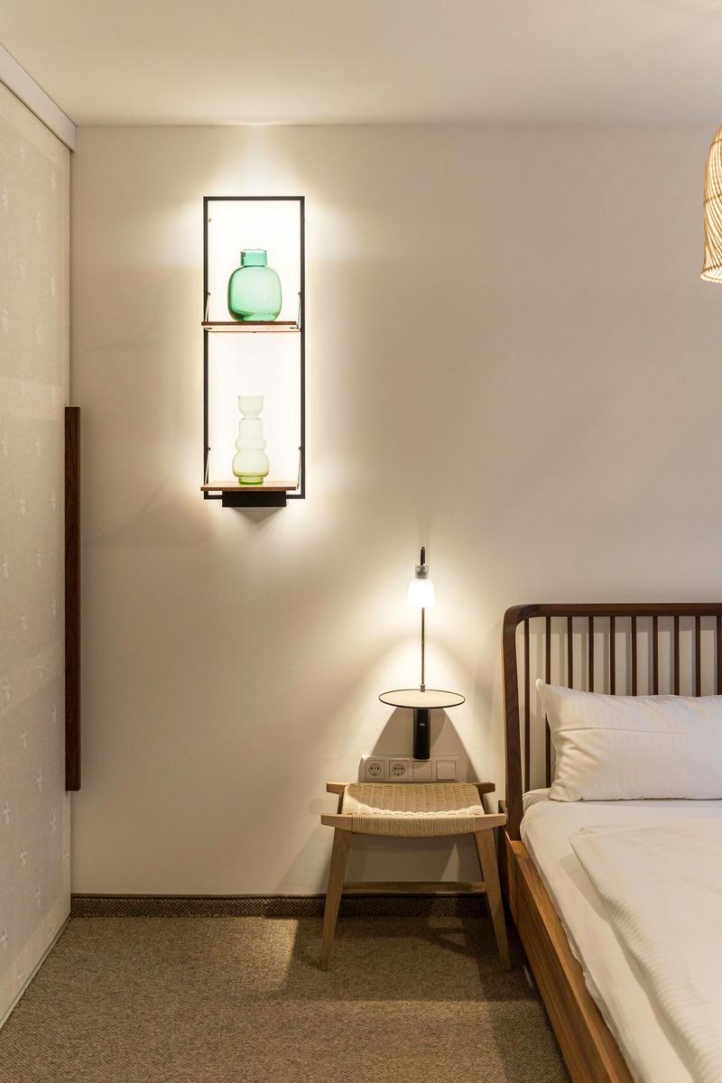 Schlafzimmer mit Bett, Nachttisch und Wandregal mit Vasen.