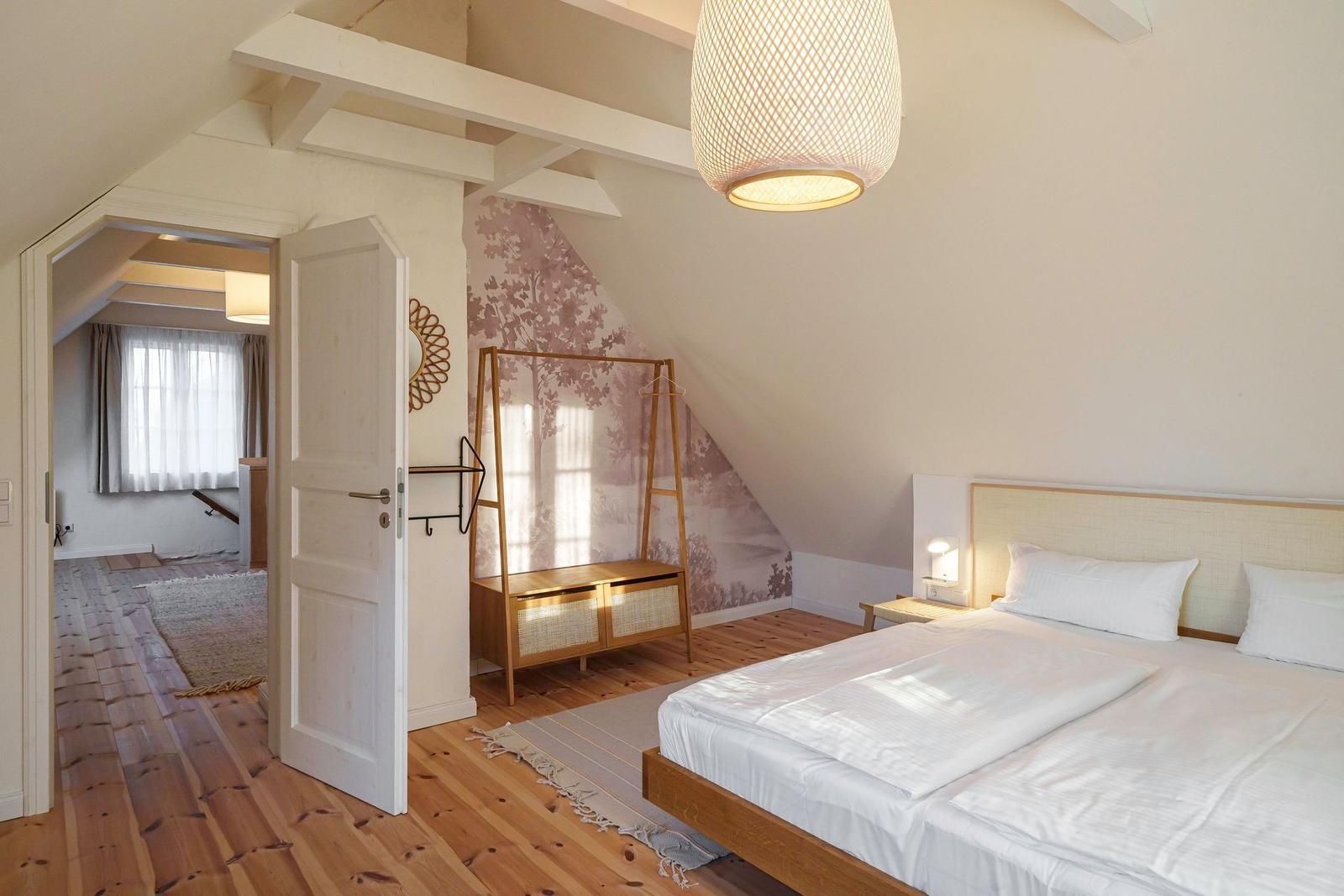 Schlafzimmer mit Dachschräge, Bett, Kleiderständer und Tür zu angrenzender Raum.