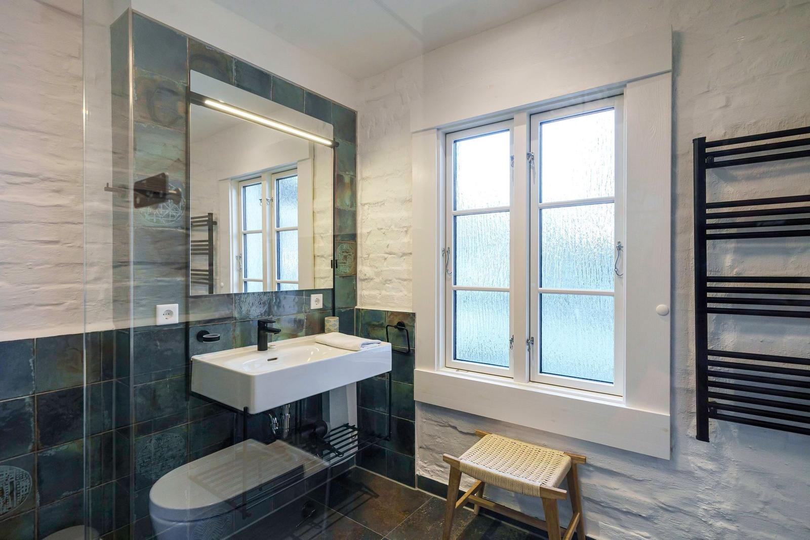 Badezimmer mit Waschbecken, Spiegel, Toilette und Fenster.