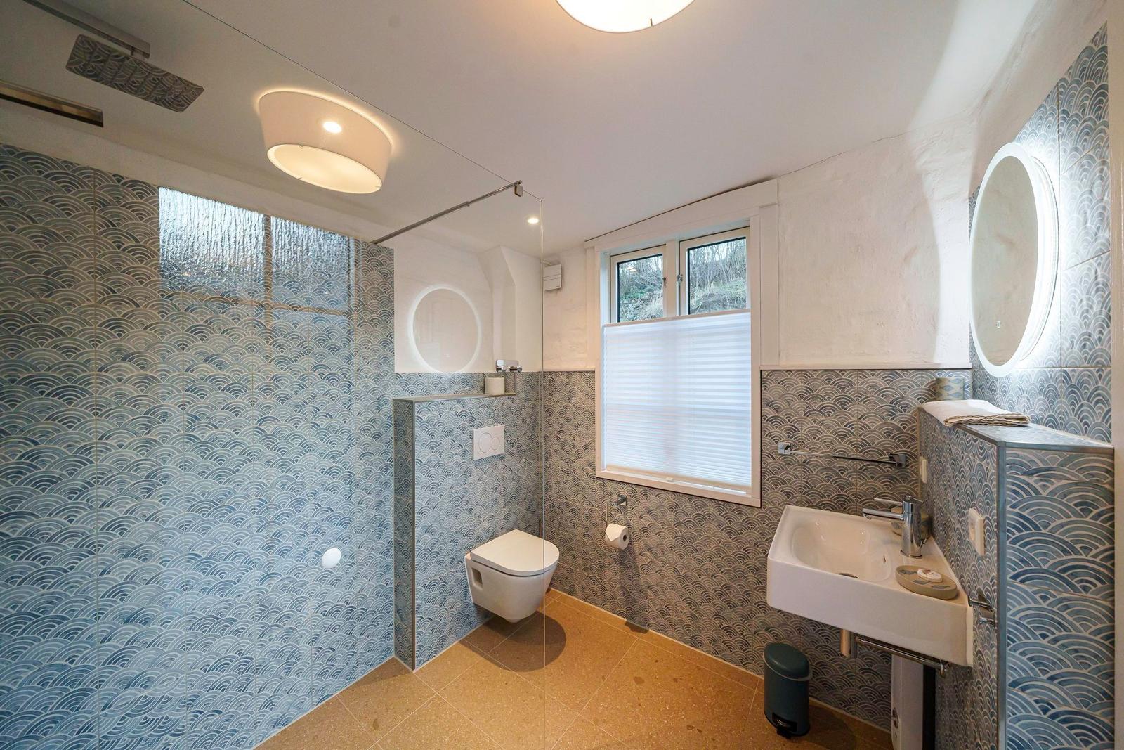 Badezimmer mit Dusche, Waschbecken und Toilette. Wände mit Wellenmustertiles.