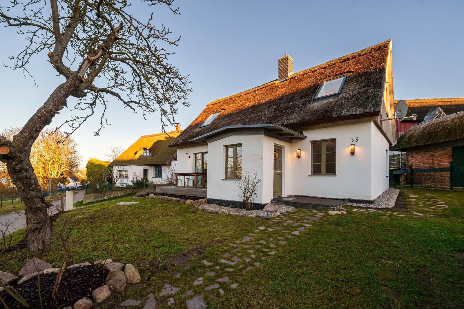 Wohnhaus mit Strohdach, weißer Fassade und Gartenweg. Hausnummer 33.