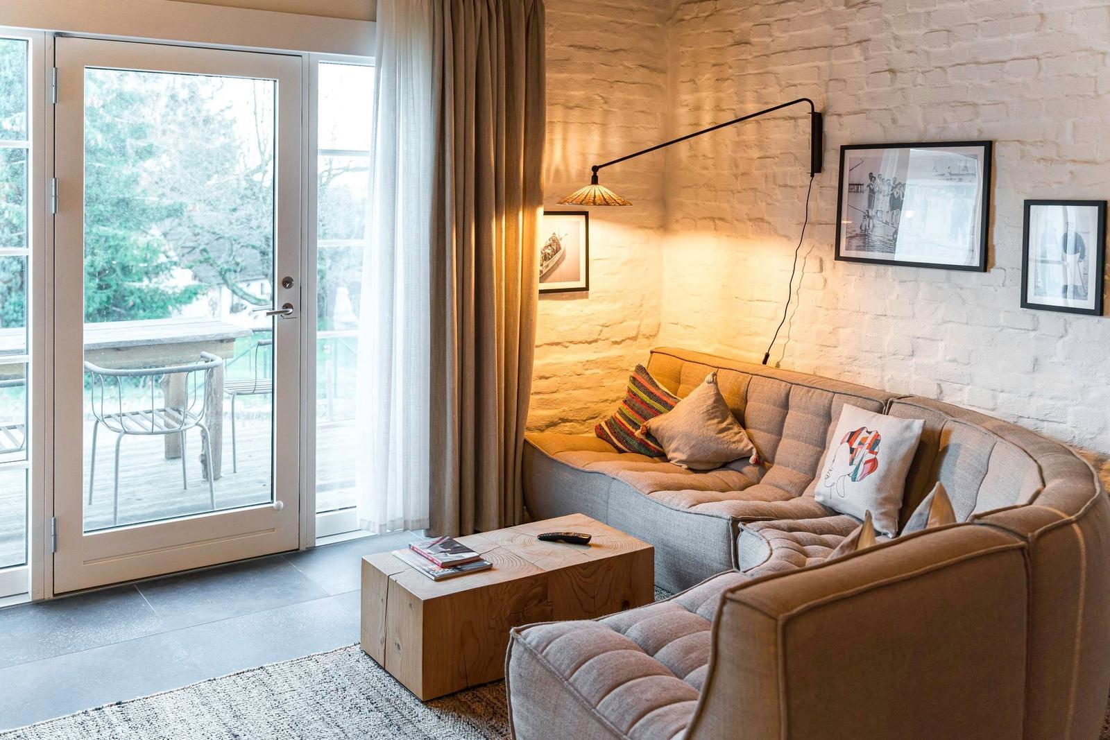 Ein Wohnbereich mit Sofa, Tisch und Terrassentür. Weiße Ziegelwand und Bilder.