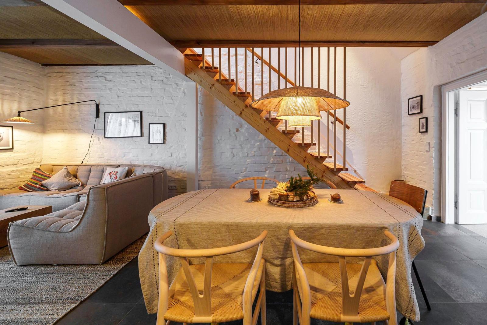 Essbereich mit Tisch und Stühlen, dahinter Wohnbereich mit Sofa und Treppe.