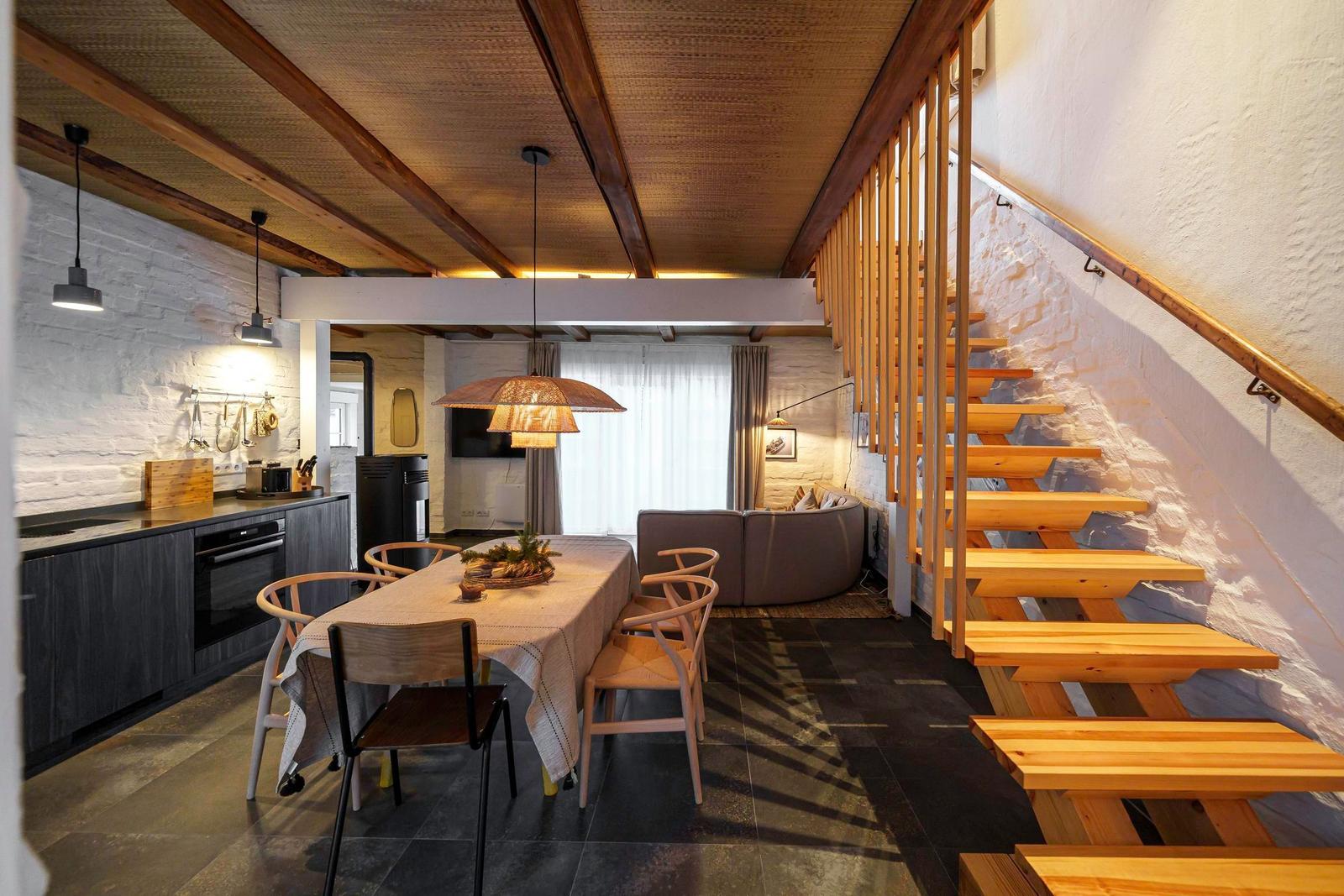 Essbereich mit Tisch, Stühlen und Küchenzeile. Holztreppe führt zur oberen Etage.