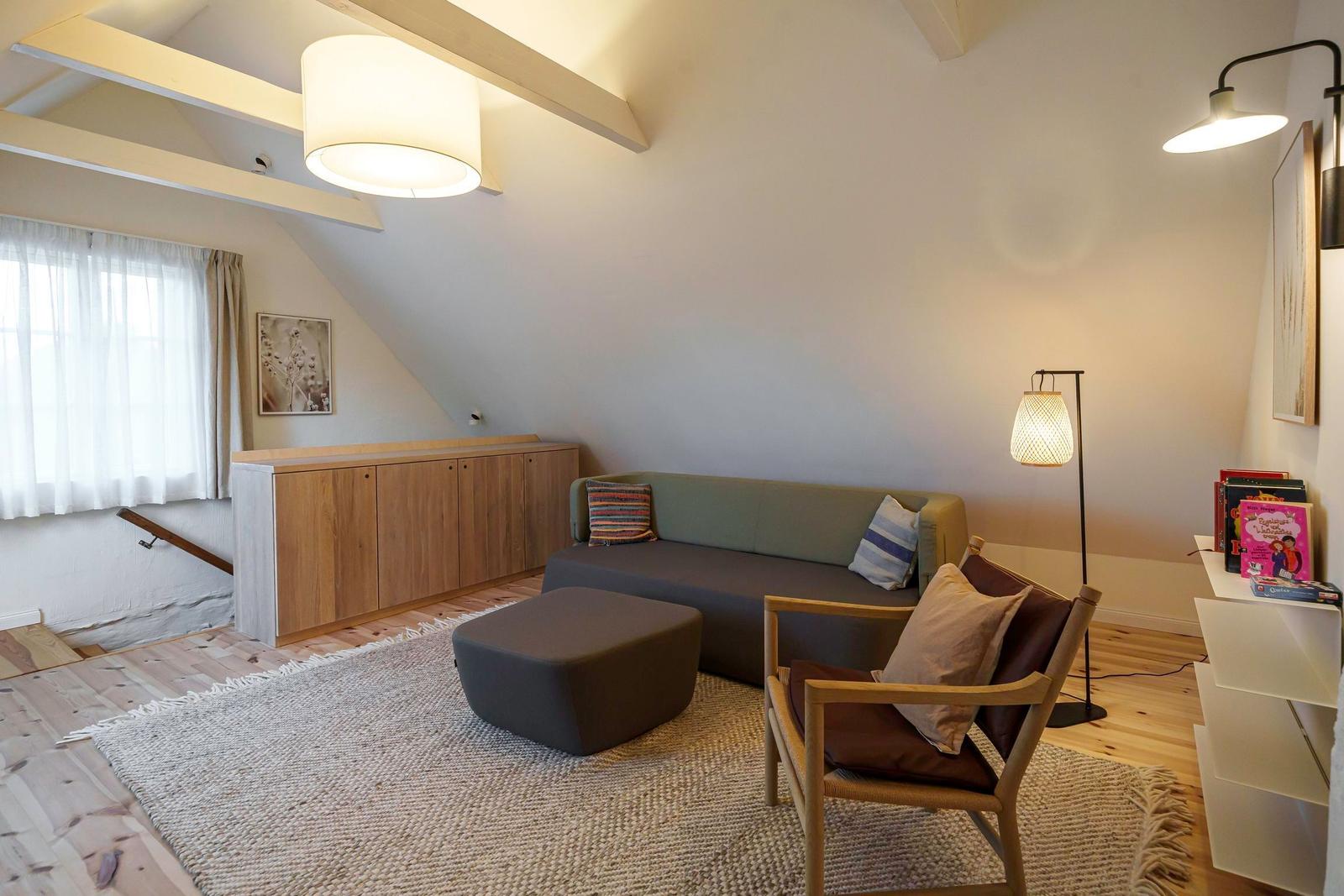 Wohnraum mit Sofa, Sessel und Holzboden unter schrägen Dachschrägen.