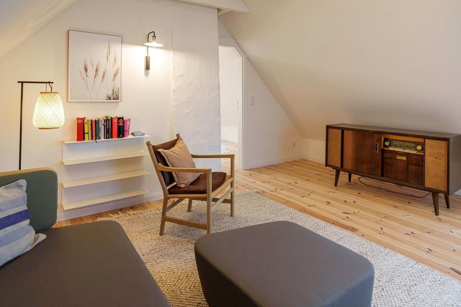 Wohnraum mit Holzboden, Sessel, Couch und Radio-Schrank unter Dachschrägen.