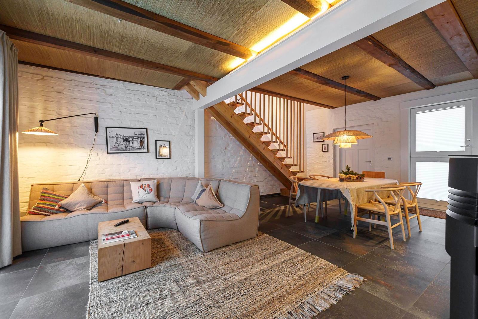 Wohn- und Essbereich mit Sofa, Tisch und Stühlen unter Holzbalkendecke.