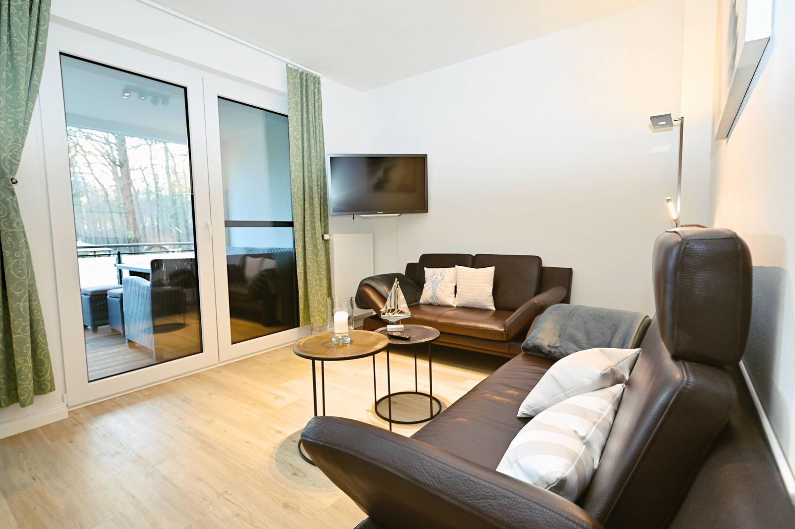 Wohnzimmer mit braunen Ledersofas, Fernseher und bodentiefen Fenstern zur Terrasse.