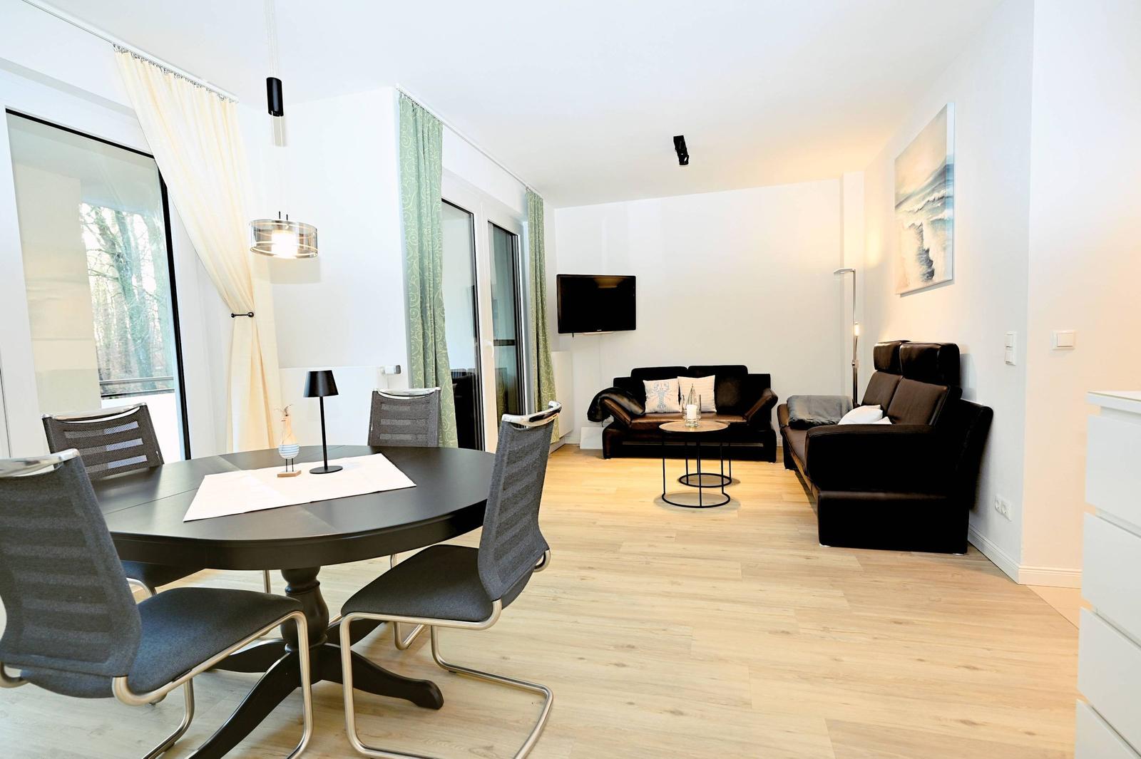 Wohn- und Essbereich mit Esstisch, Sofa und Fernseher. Holzboden und große Fenster.