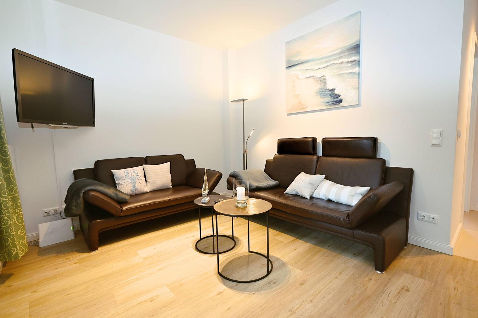 Wohnzimmer mit zwei Ledersofas, Fernseher und Wandbild.