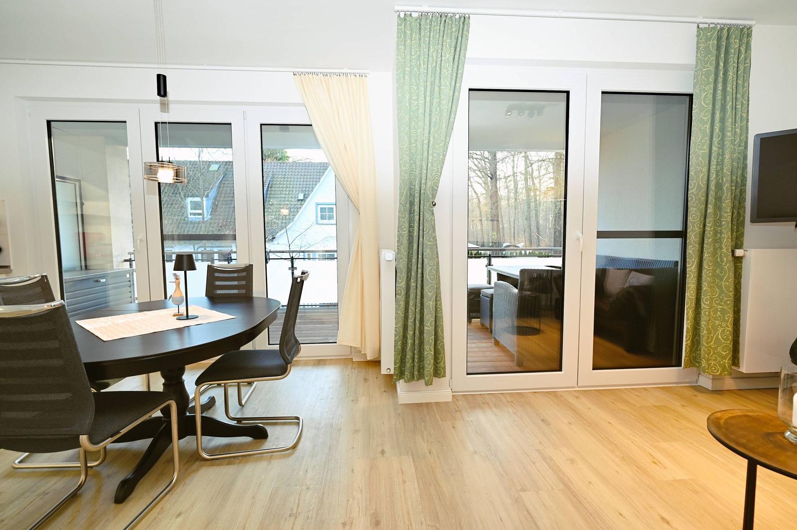 Essbereich mit Tisch und Stühlen, Durchgang zu Terrasse mit Sitzgruppe und Blick auf Wald.