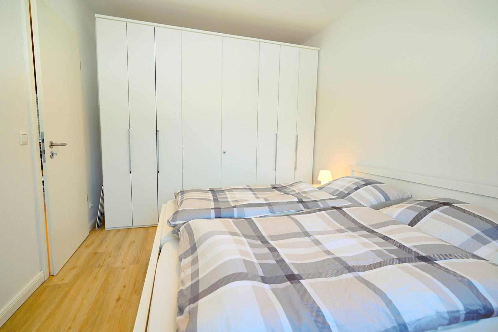 Schlafzimmer mit Doppelbett, weißem Schrank und Holzboden.