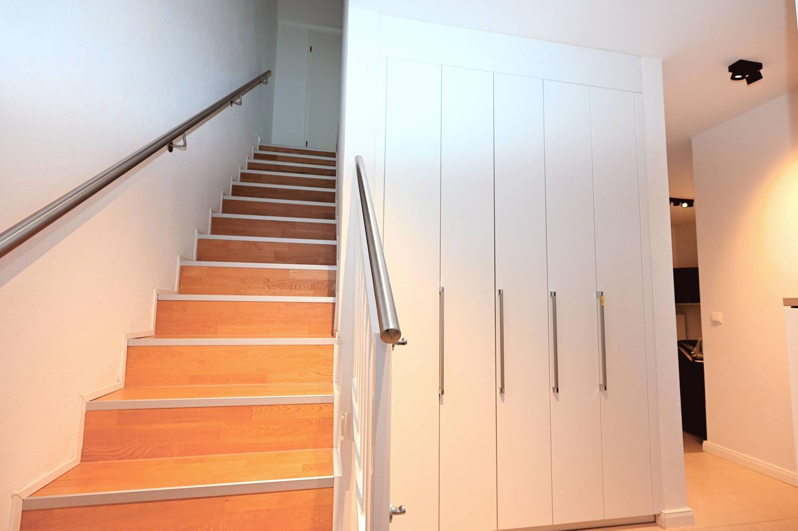 Helle Treppe mit Holzstufen und Metallgeländer neben weißen Schranktüren.