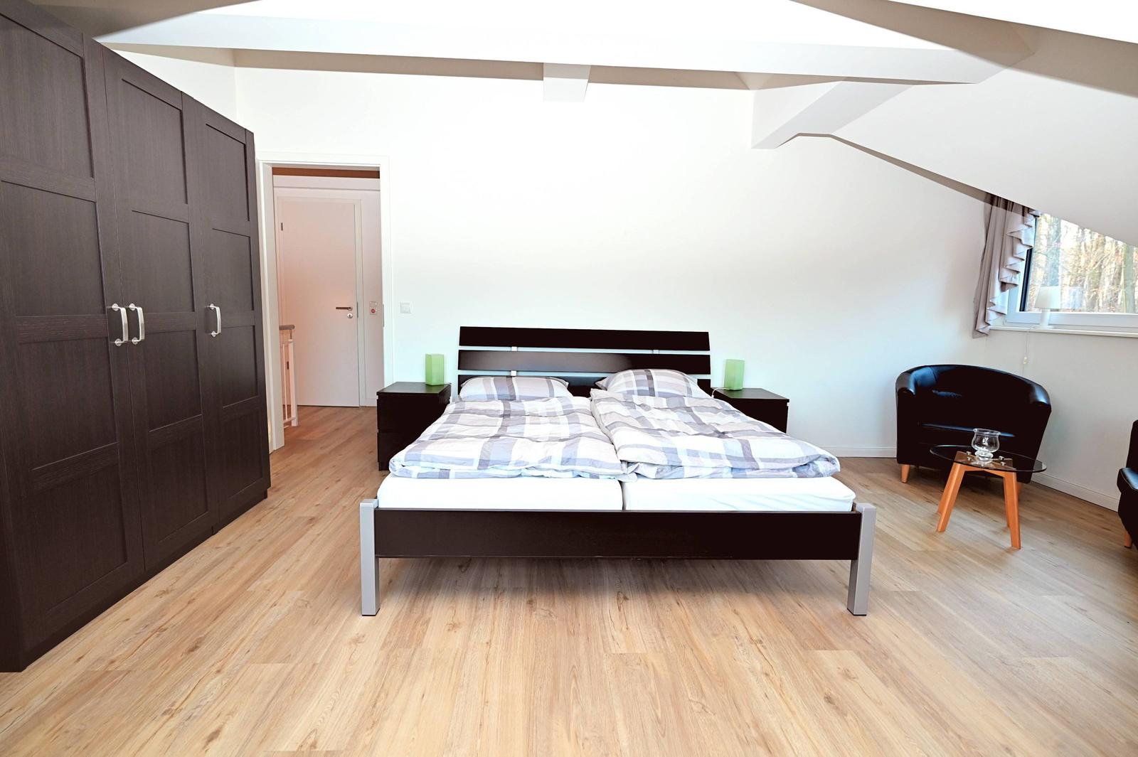 Schlafzimmer mit Doppelbett, Kleiderschrank und Sitzgelegenheit unter Dachschrägen.