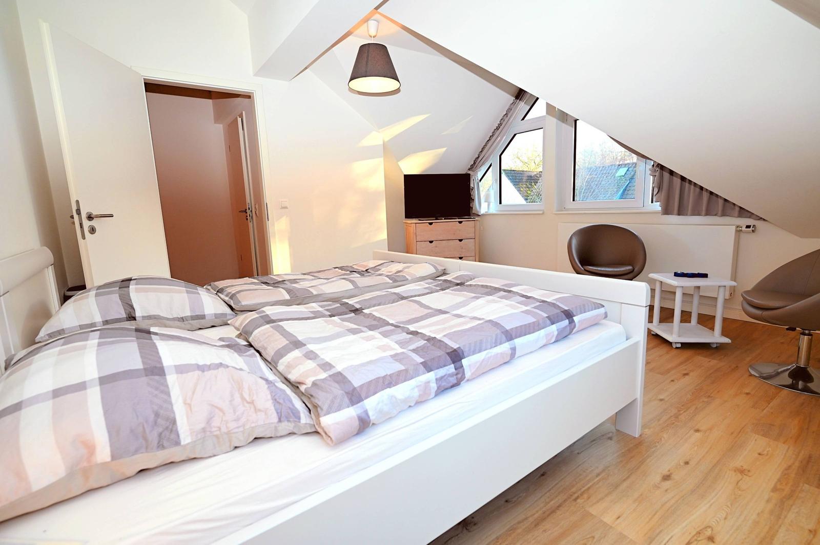 Schlafzimmer mit Dachschrägen, Bett, Fernseher und zwei Stühlen.