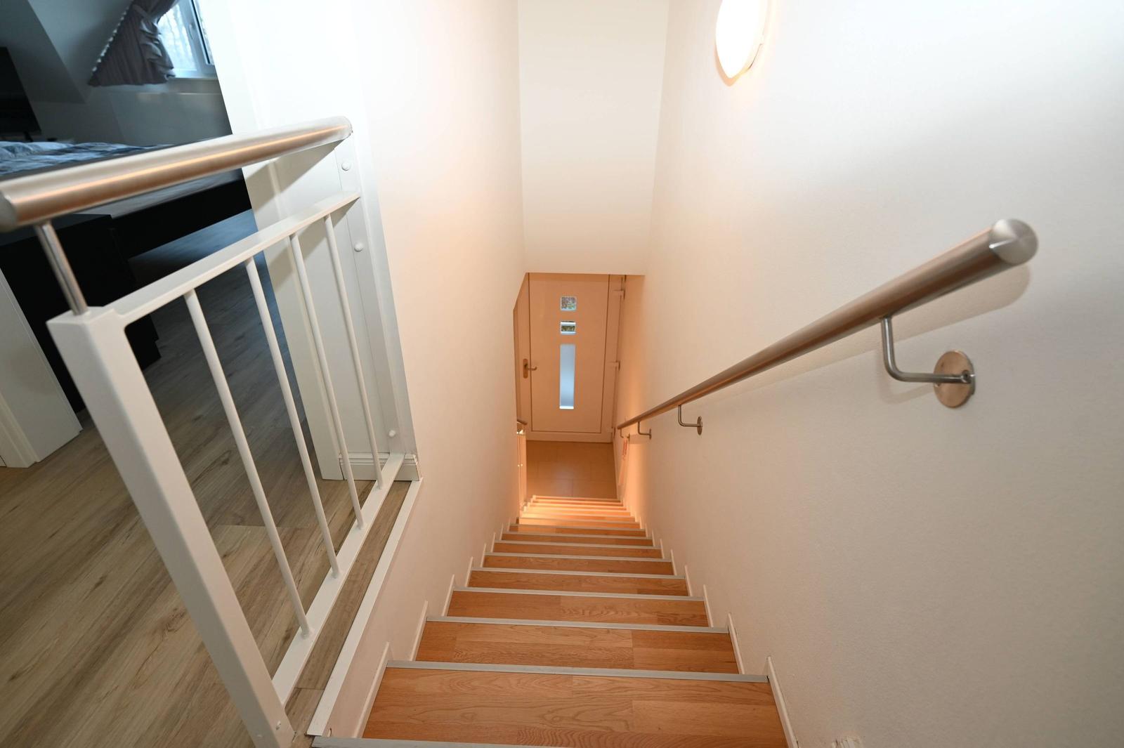 Helle Treppe mit Holzstufen und Metallgeländer führt nach oben.