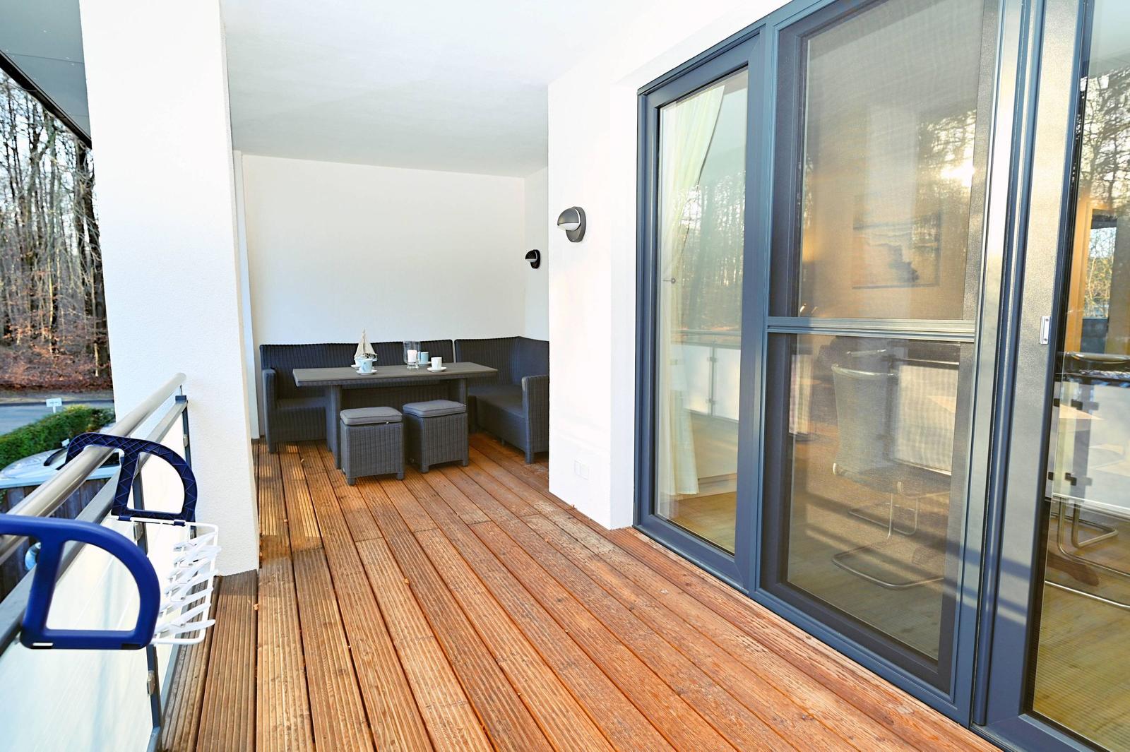 Terrasse mit Holzboden, Sitzgruppe und Tisch. Durchgehende Glastüren zum Innenraum.