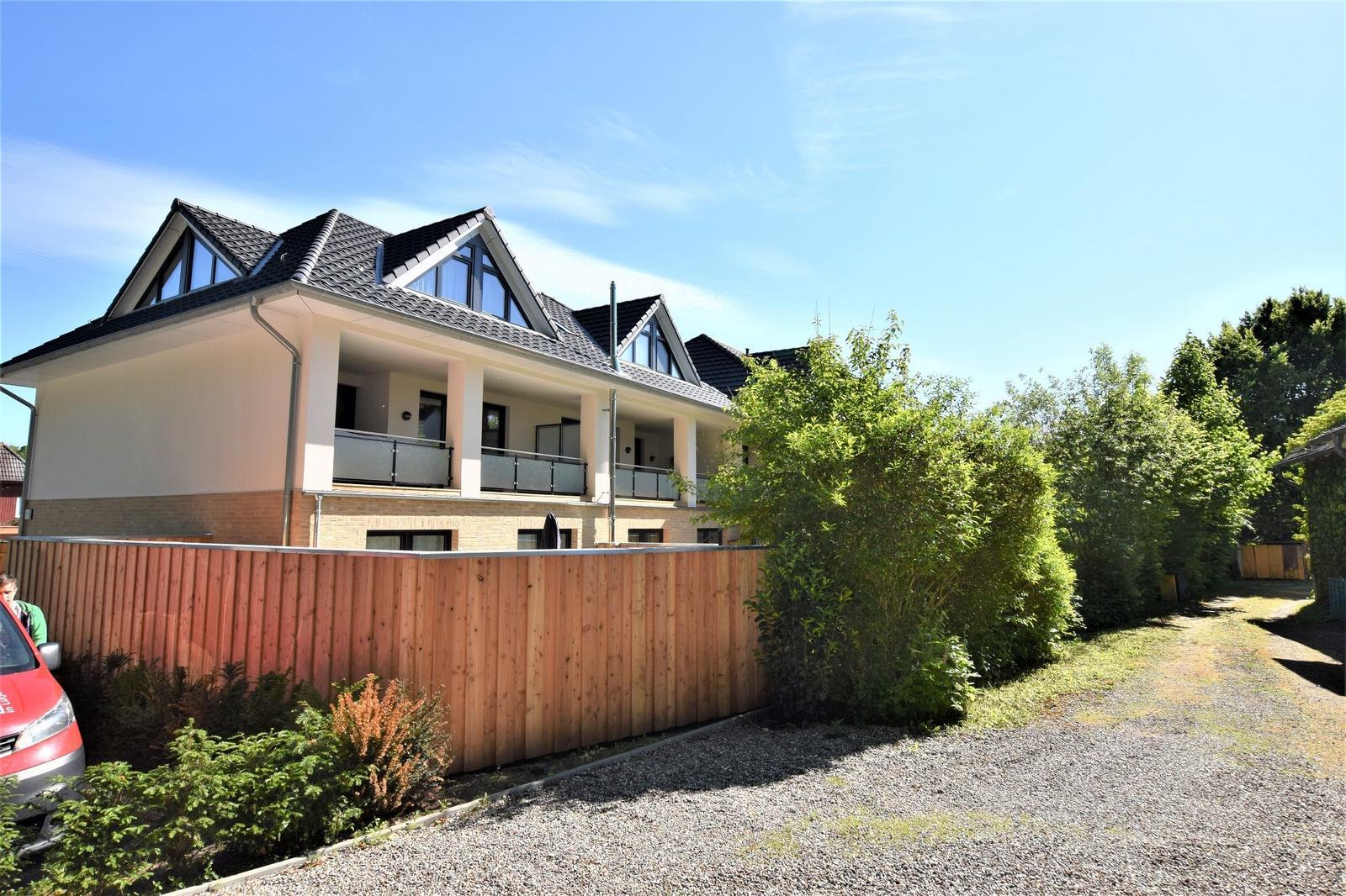 Modernes Haus mit Balkonen und Holzzaun. Grünflächen und klarer Himmel.