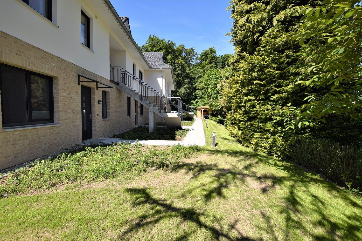 Modernes Haus mit Balkon, Gartenweg und grüner Umgebung.