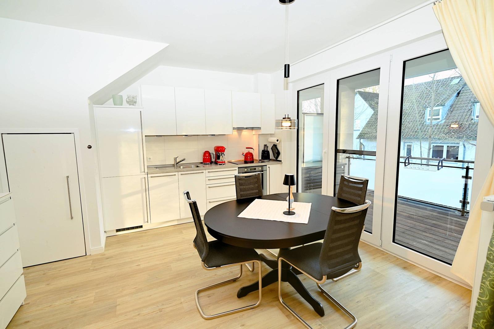 Küche und Essbereich mit runder Tisch und Stühlen. Durchgang zur Terrasse mit Glasfront.