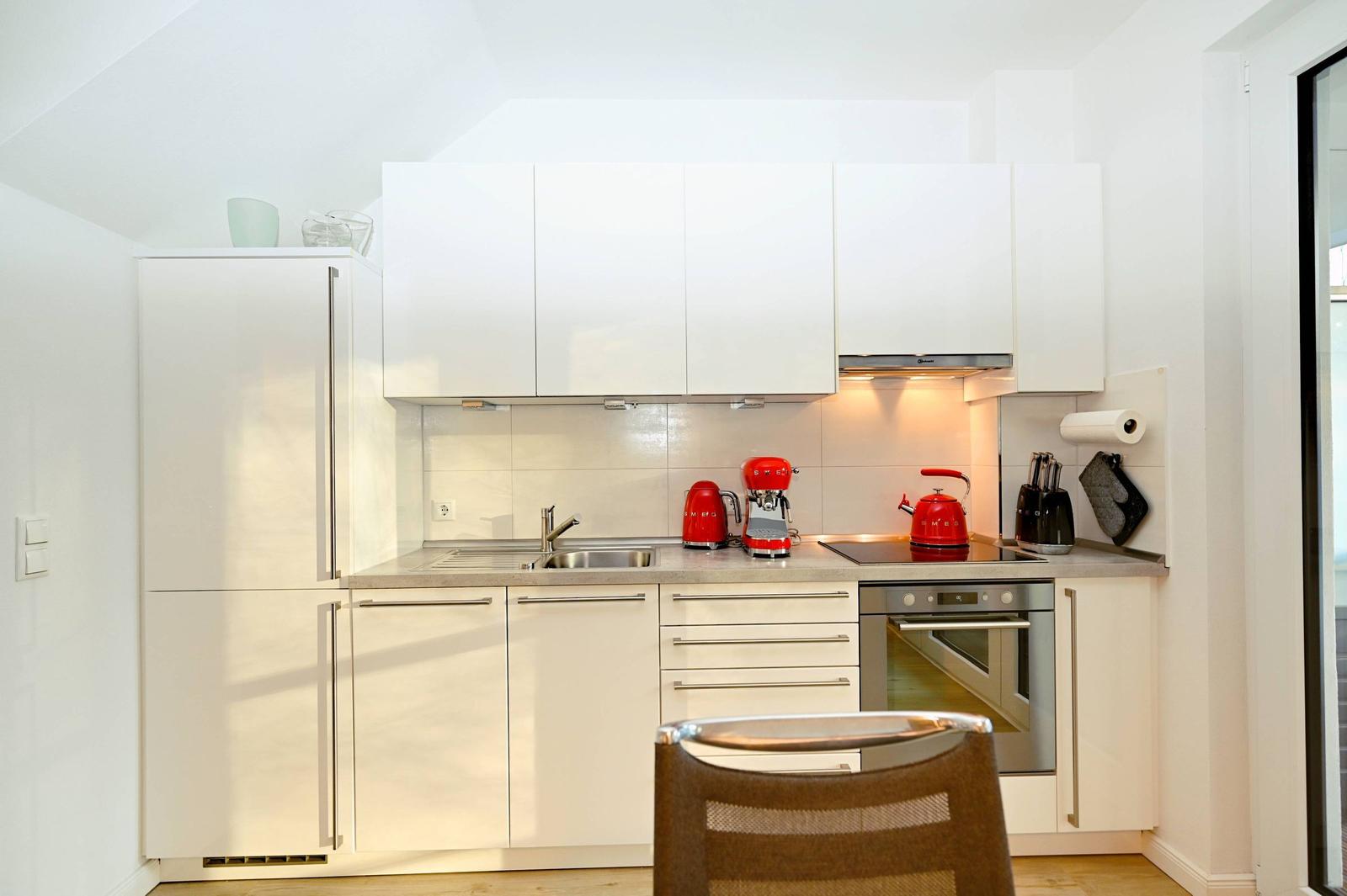 Moderne Küche mit weißen Schränken, roten Küchenutensilien und integriertem Ofen.