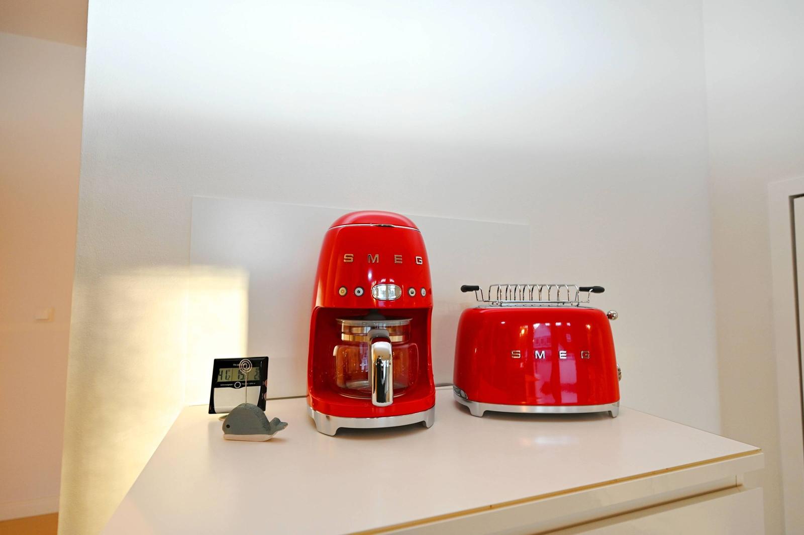 Auf der Arbeitsfläche stehen zwei rote Küchengeräte und ein kleines digitales Gerät.