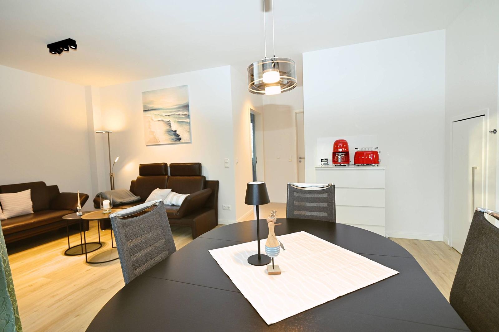 Essbereich mit runder Tisch und Stühlen. Wohnbereich mit Sofa und Wandbild.