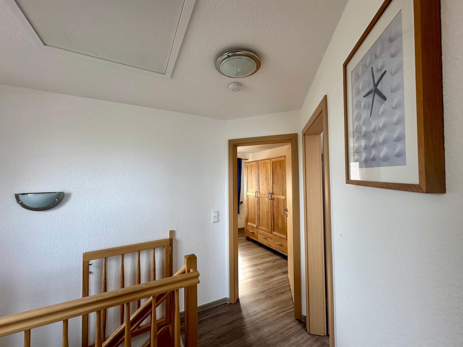Flur mit Holzgeländer, Wandbild und Blick in Schlafzimmer mit Kleiderschrank.