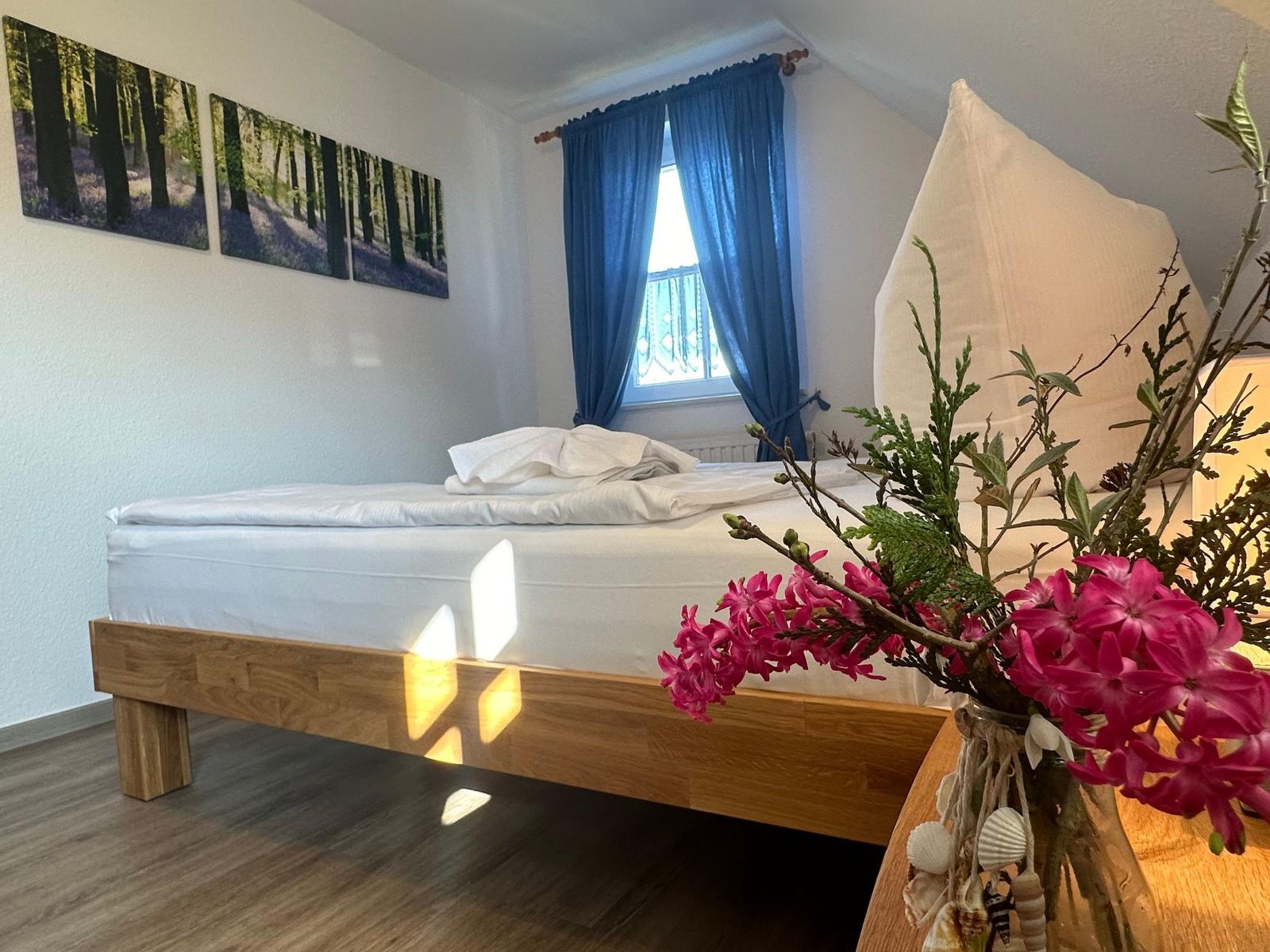 Schlafzimmer mit Holzbett, blauen Vorhängen und Wandbildern