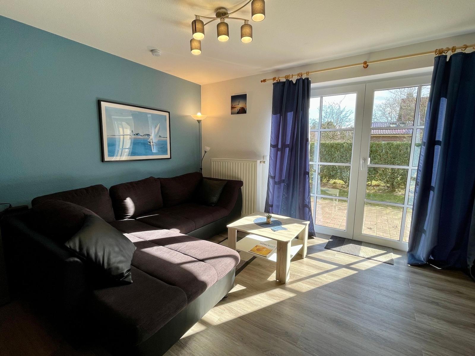 Wohnzimmer mit Sofa, Tisch und Glastür zum Garten.