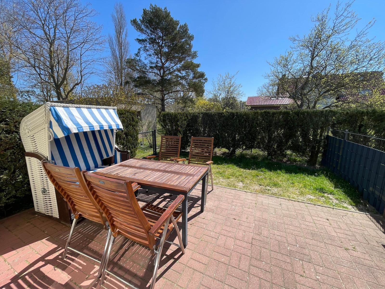 Terrasse mit Holztisch, Stühlen und Strandkorb unter blauem Himmel.