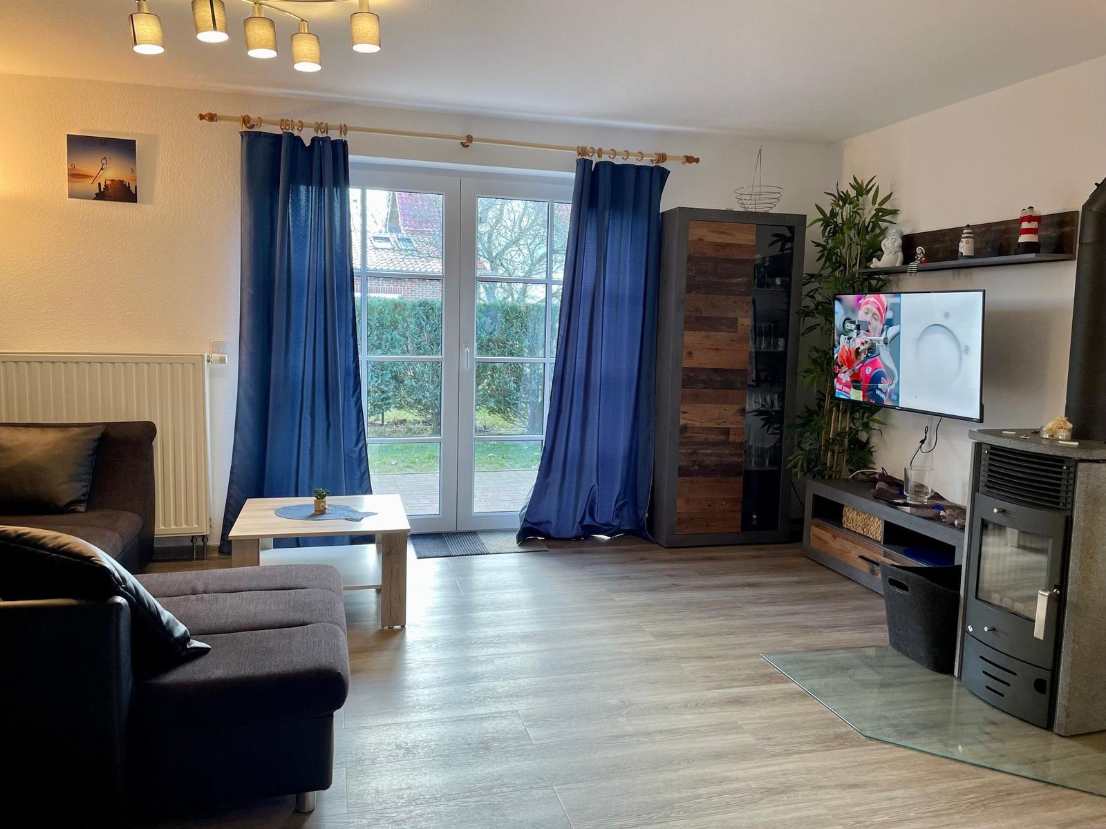 Wohnzimmer mit Sofa, TV und Fenster zur Außenterrasse.