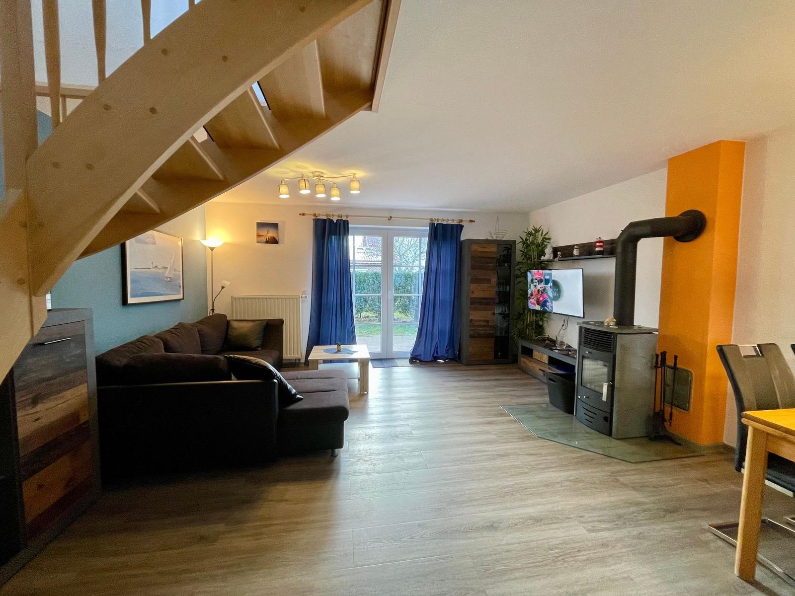 Wohnzimmer mit Sofa, TV und Kaminofen. Holztreppe und Terrassentür.