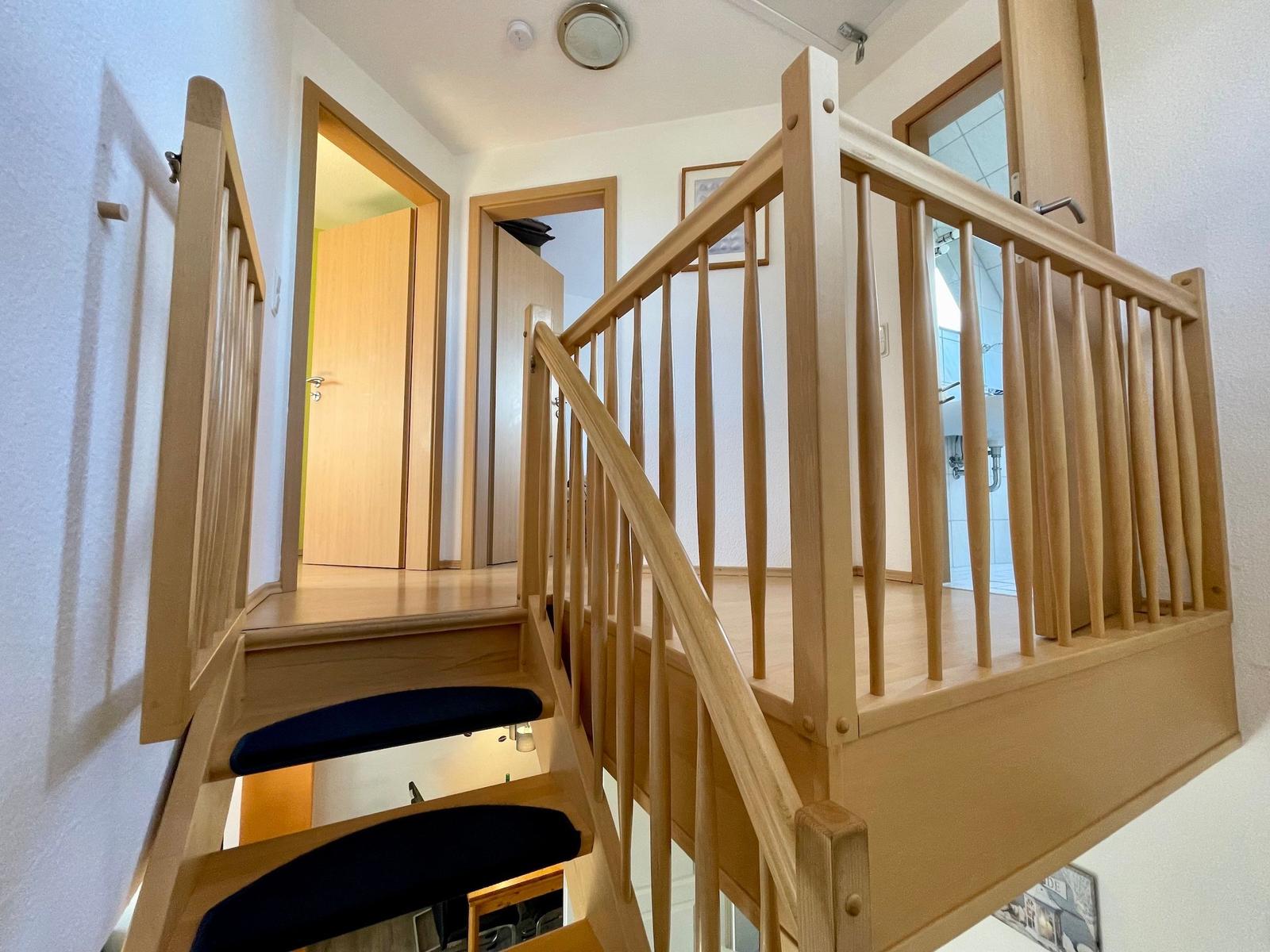 Holztreppe mit schwarzen Stufen und Geländer führt zur oberen Etage.