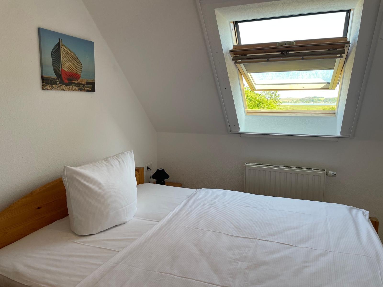 Schlafzimmer mit Dachfenster und Bett. Wandbild zeigt ein Boot.