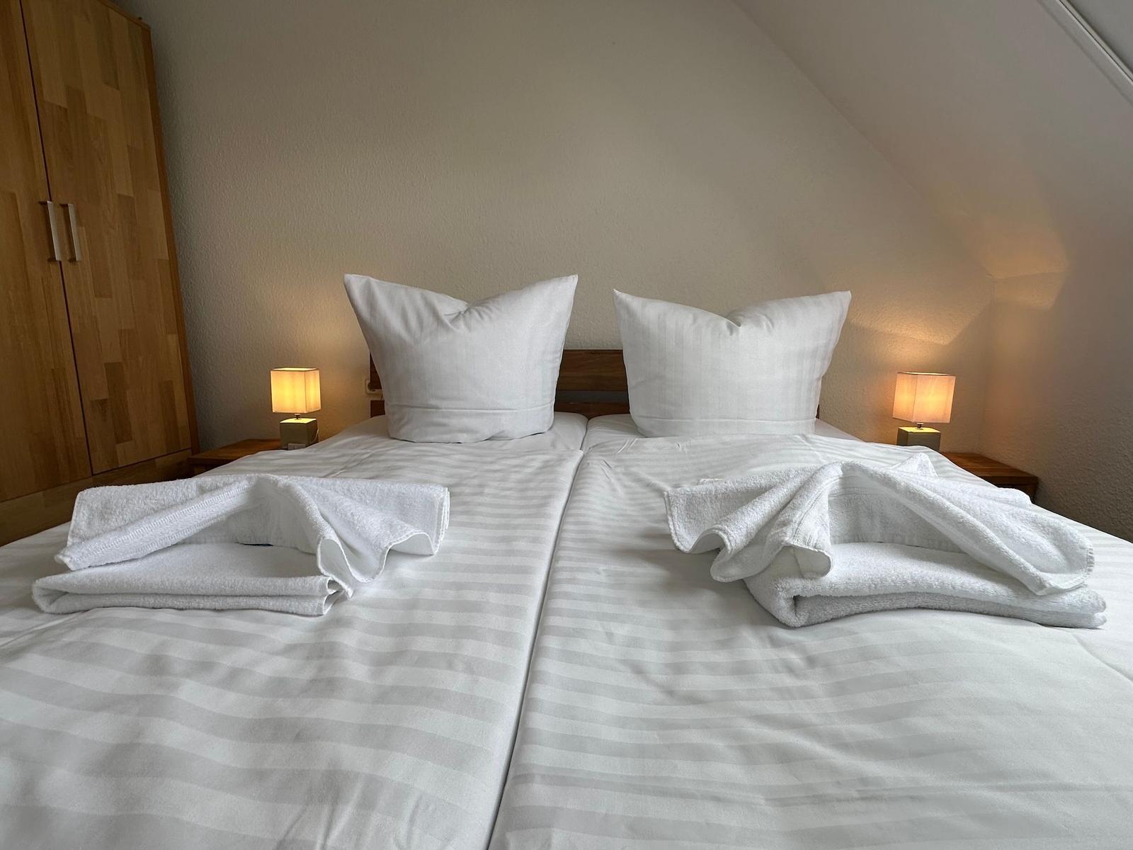 Zwei Betten mit weißen Laken und Handtüchern. Beide Nachttische mit Lampen.