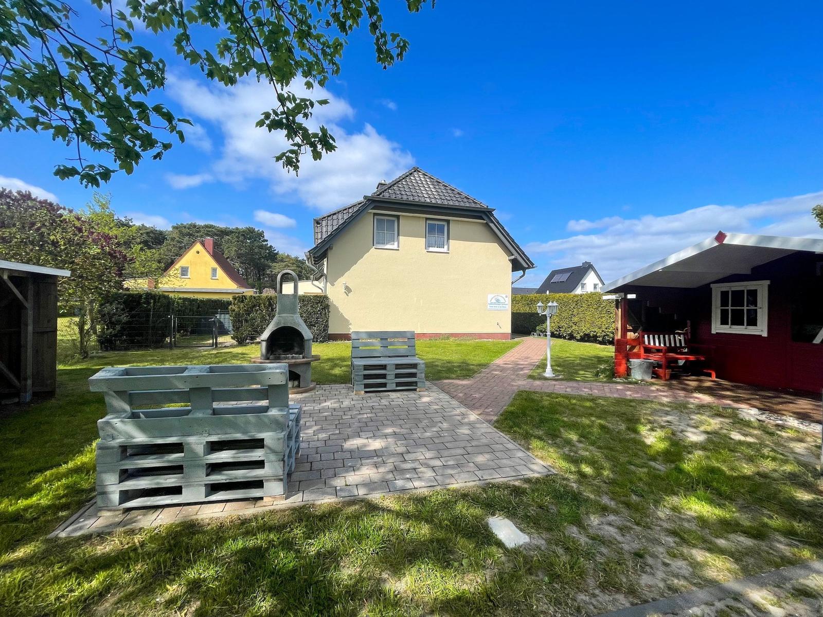 Haus mit Garten, Grill und Holzbank unter blauem Himmel.