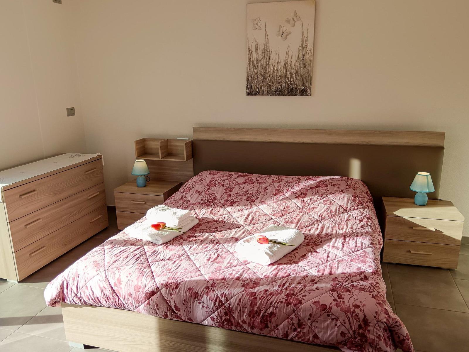 Schlafzimmer mit Bett, Nachttischen und Schrank. Auf dem Bett liegen Handtücher und Tulpen.