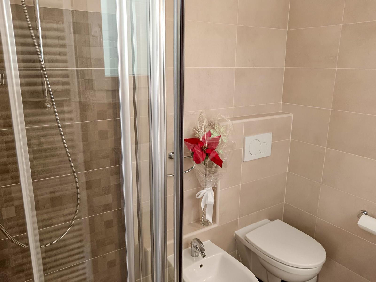 Badezimmer mit Dusche, Waschbecken und Toilette. Blume als Dekoration.