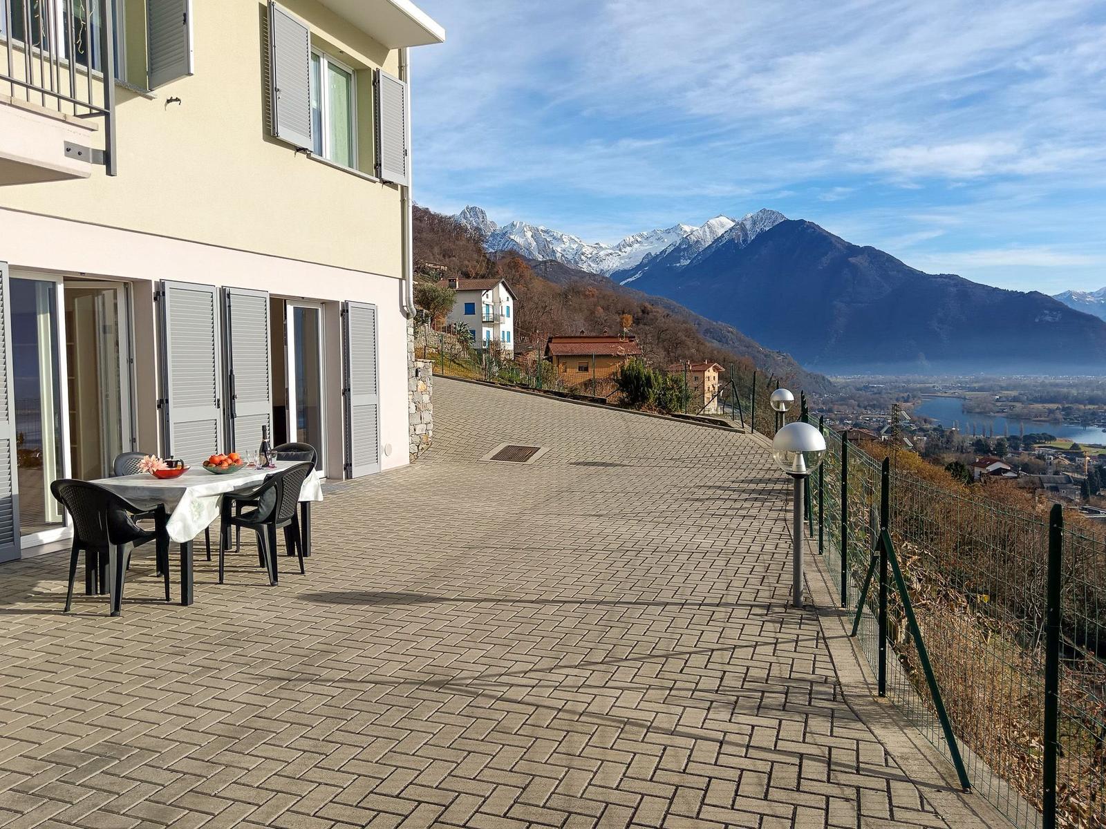 Terrasse mit Tisch und Stühlen, Blick auf Berge und See.